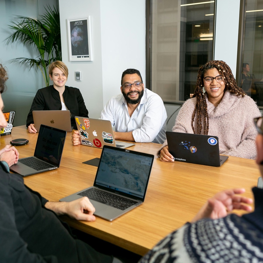 A leadership team around a conference table, several with open laptops, working through a discussion